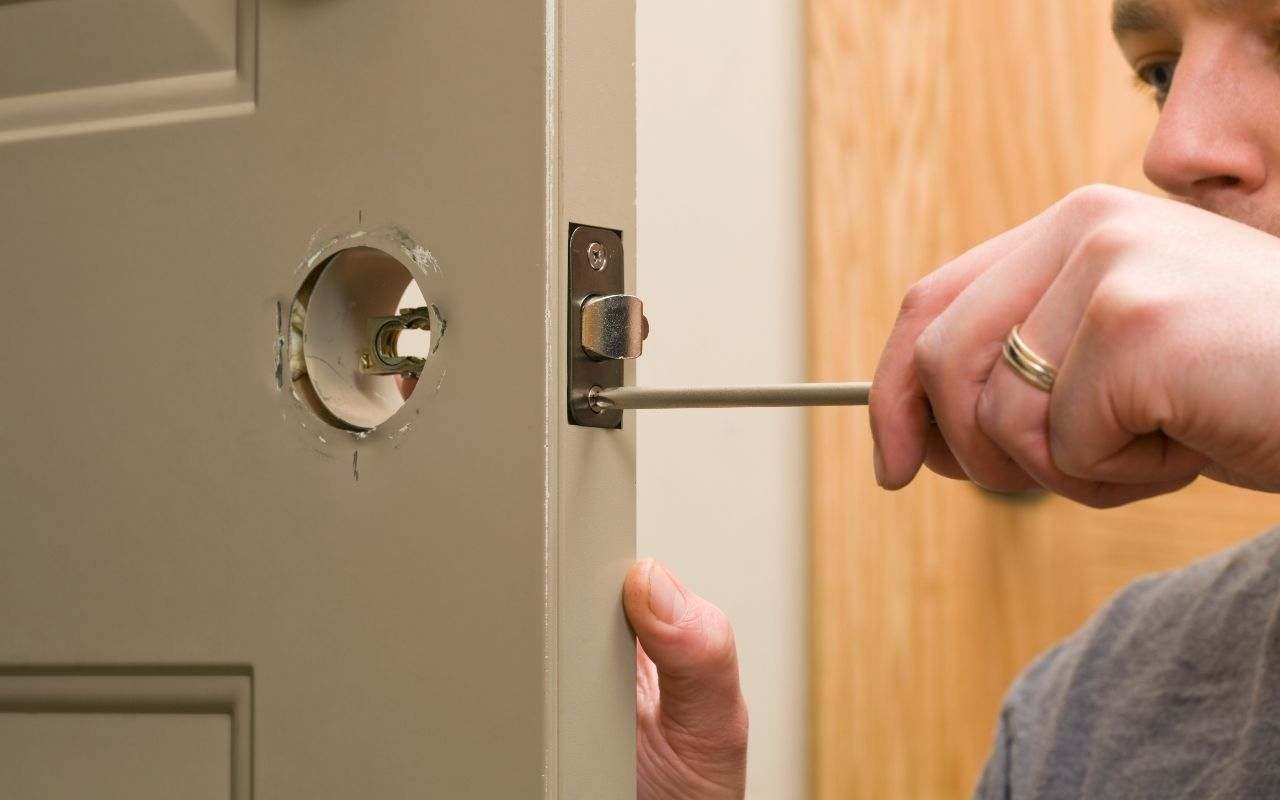 A professional replacing a commercial door handle on a metal door.